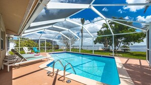 A covered swimming pool with lounge chairs and a view of the sea. - Picturesque Watefront, Heated Pool, Ping Pong Table - Villa Sunset Riverhouse - Roelens Vacations (Cape Coral)