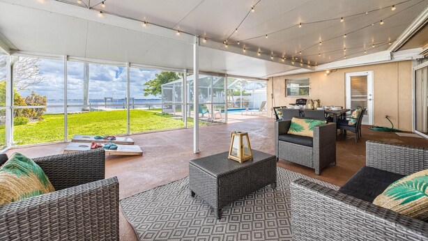 An outdoor patio with wicker furniture, a glass enclosure, and a view of the ocean. - Picturesque Watefront, Heated Pool, Ping Pong Table - Villa Sunset Riverhouse - Roelens Vacations (Cape Coral)