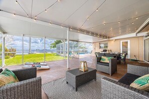 Une terrasse extérieure dotée de meubles en osier, d’une véranda en verre et offrant une vue sur l’océan.