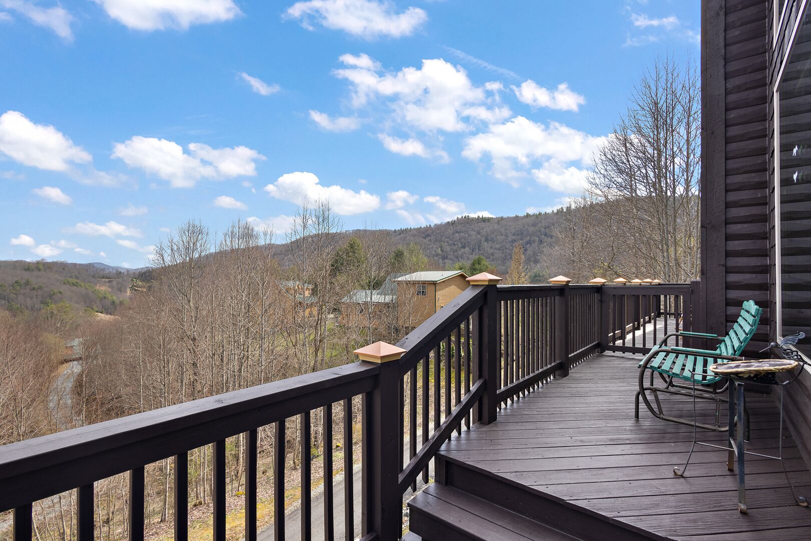 A wooden deck with a railing, two green chairs, and a small table.