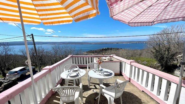 Een terras met twee tafels, stoelen en gestreepte parasols met uitzicht op een waterpartij.