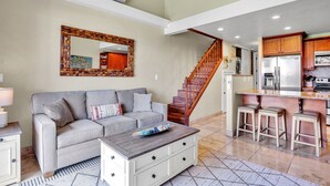 Ein geräumiges Wohnzimmer mit grauem Sofa, Holztisch und einer Treppe, die in einen Küchenbereich führt.