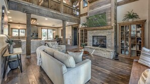 A spacious living area with a high ceiling, a fireplace, and a large window overlooking a football field.