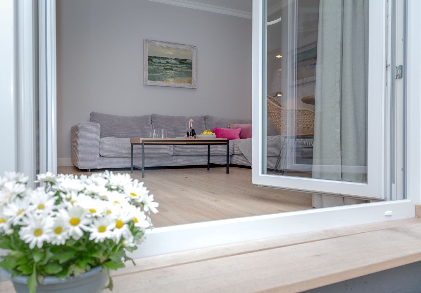 A modern living room with a grey sofa, a coffee table, and a glass door leading to a balcony.