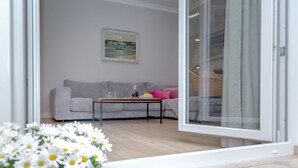 A modern living room with a grey sofa, a coffee table, and a glass door leading to a balcony.