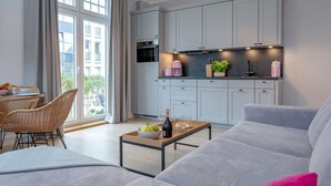 A modern living room with a sofa, a dining table with chairs, and a kitchen area with cabinets and appliances.