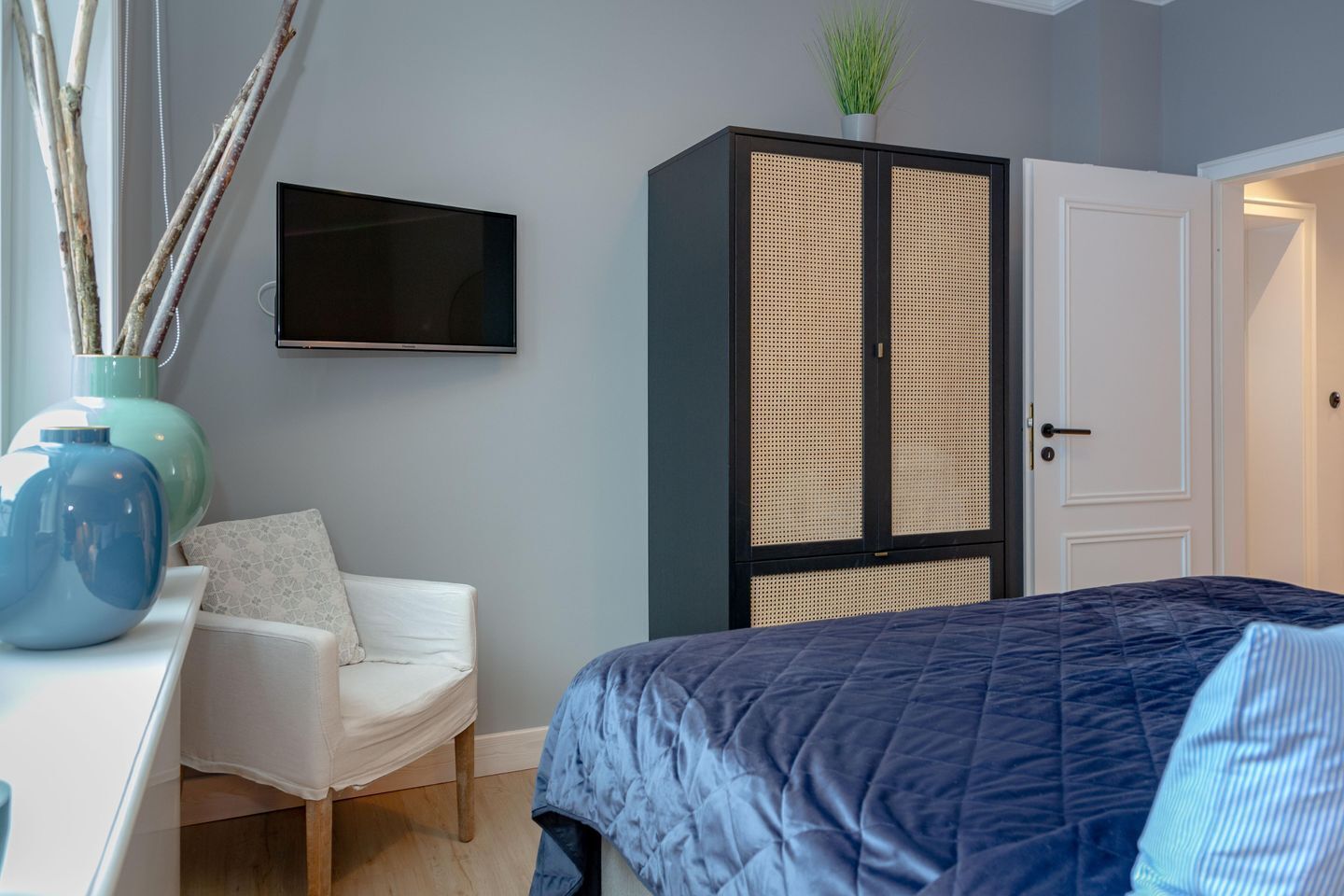 Une chambre à coucher avec un lit, une chaise blanche, un téléviseur et une armoire.