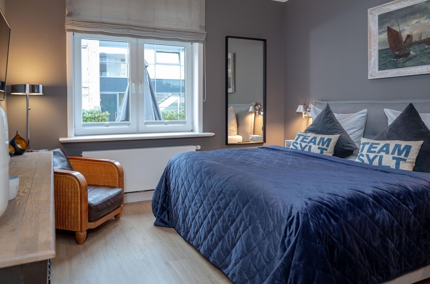 Un dormitorio con una cama grande, una ventana con cortinas, una silla, una lámpara y un cuadro en la pared.