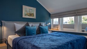Un dormitorio con una cama grande, un cuadro sobre la cama, una ventana con persianas y una mesita de noche con una lámpara.