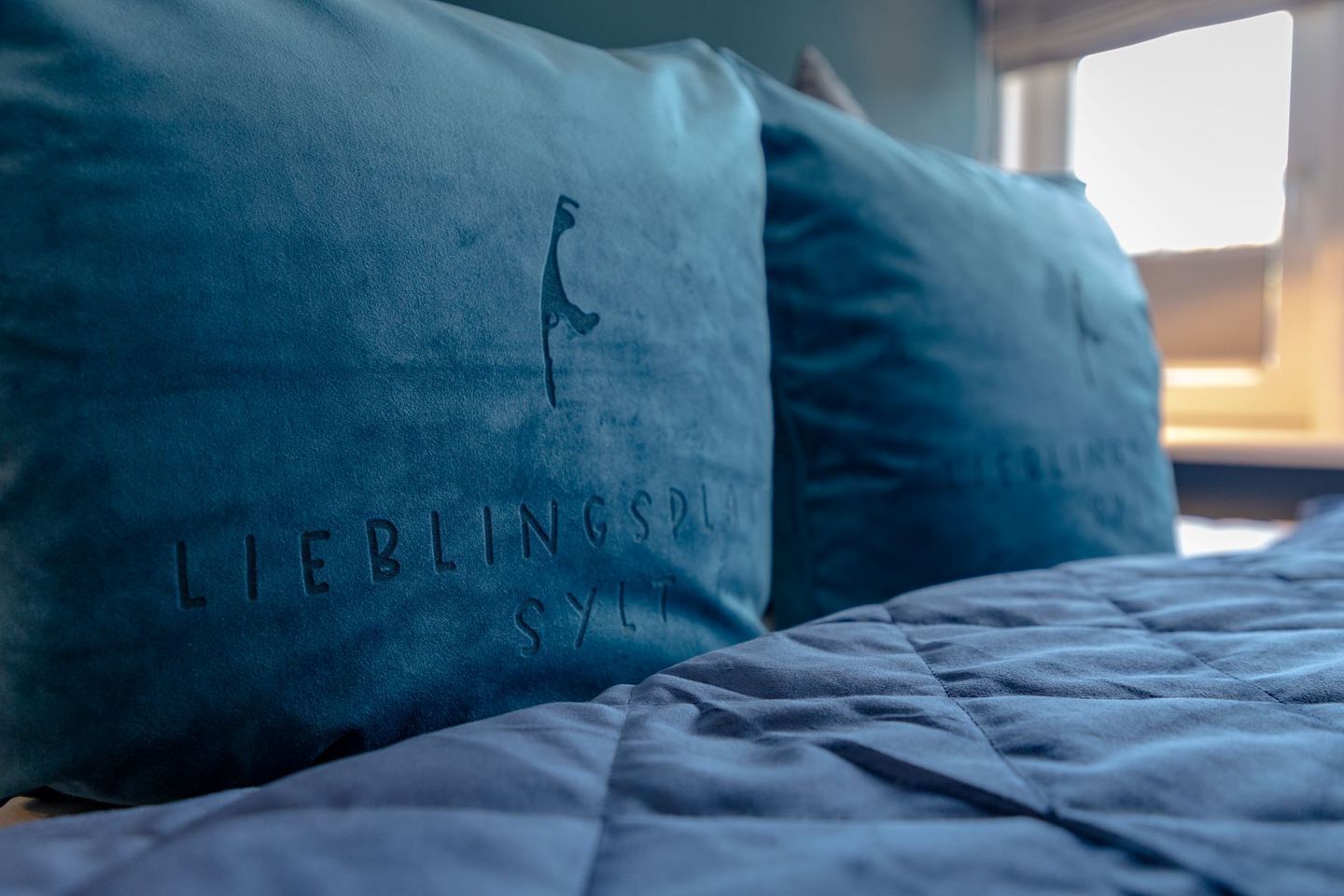 Un lit avec une couette bleue et des oreillers ornés du texte « LIEBLINGS SYLL » et de la silhouette d’une girafe.