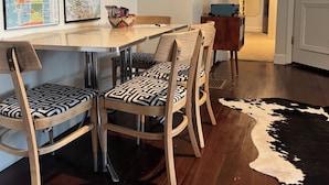 Een eetgedeelte met een houten tafel en stoelen, een vachttapijt en wandkaarten.