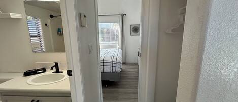 Un pasillo que conduce a un dormitorio con una cama, un baño con lavamanos y espejo, y una puerta con un número.