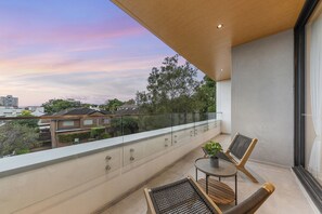Relax on the balcony with a view of the surrounding residential area, featuring a glass railing and a flat roof.