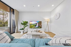 Relax in this serene space with a large window offering a view of the surrounding trees, a comfortable sofa, and a flat-screen TV.