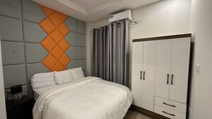 A bedroom with a bed, a wardrobe, and an air conditioning unit. - Seven Heaven Plaza (Brufut)