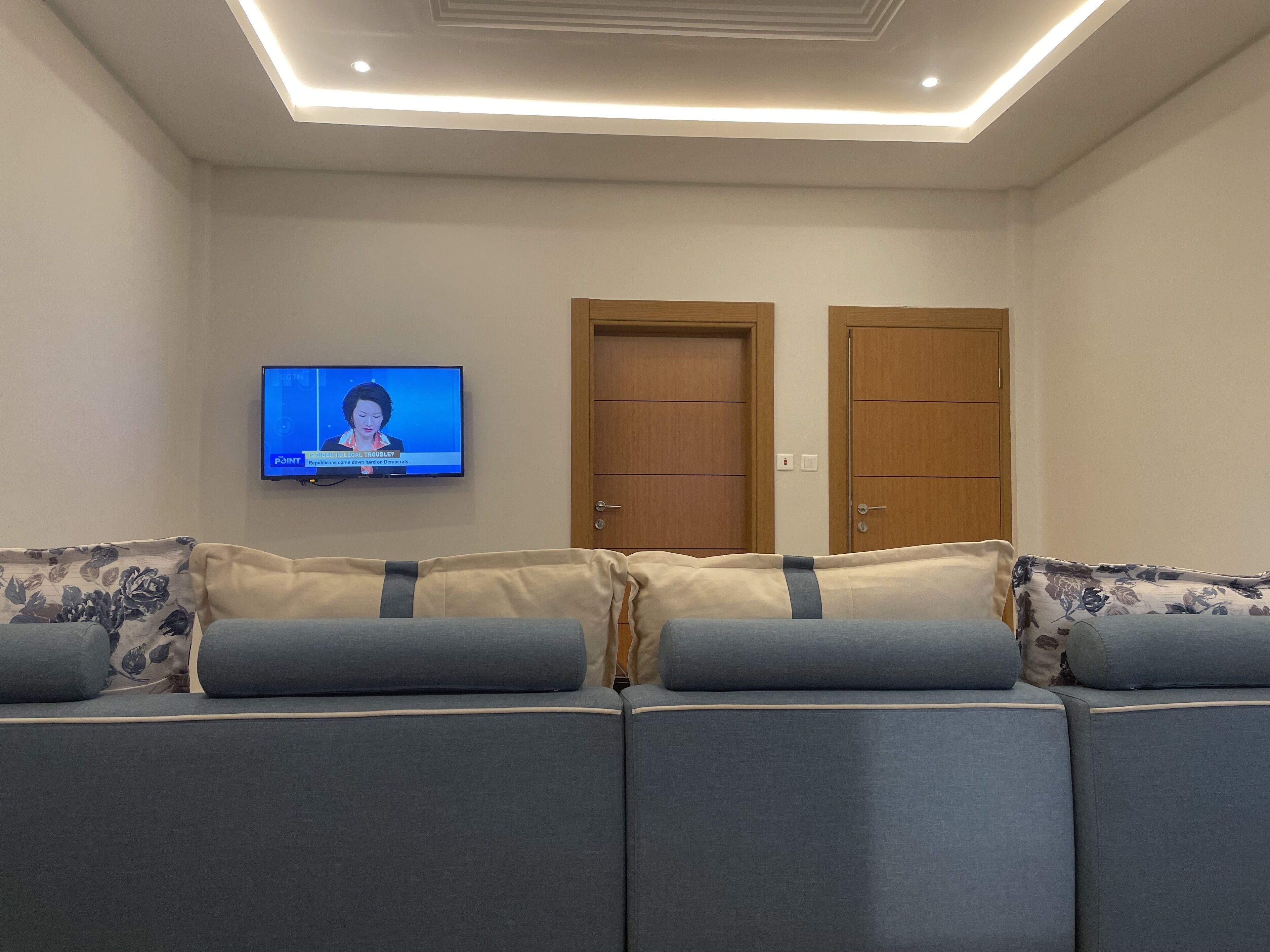A living room with a sofa, a television mounted on the wall, and two wooden doors.