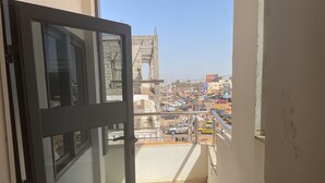 A narrow corridor with a glass door leading to a balcony overlooking a busy street with cars and buildings. - Seven Heaven Plaza (Brufut)