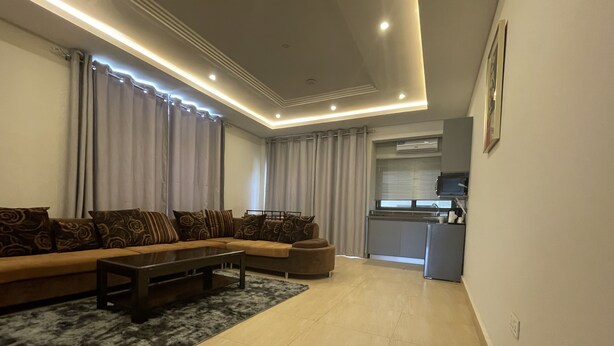 A modern living room with a sectional sofa, a coffee table, and a rug. - Seven Heaven Plaza (Brufut)