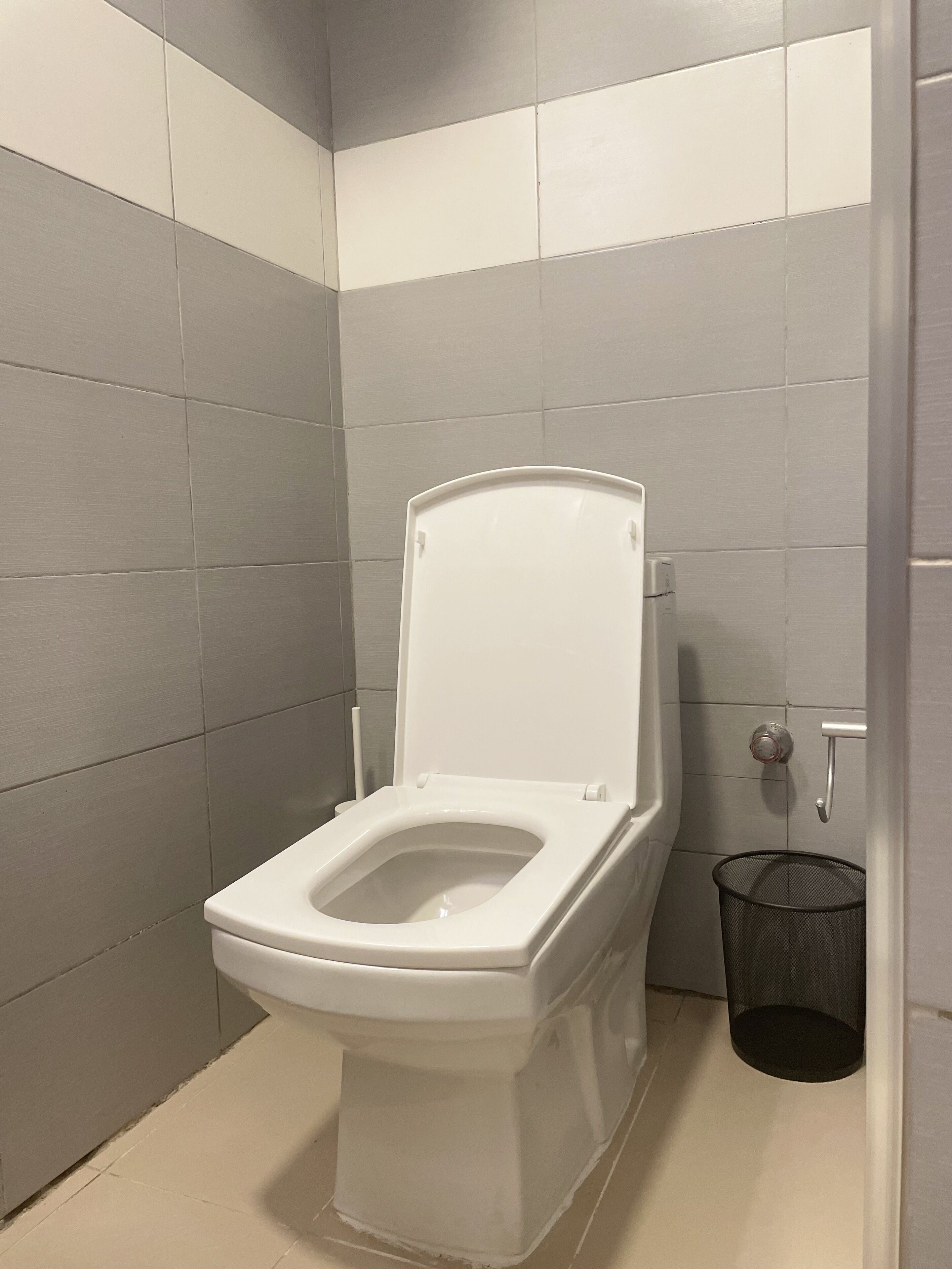 Ein modernes Badezimmer mit Toilette in Weiß, grauen Fliesenwänden und einem schwarzen Mülleimer.