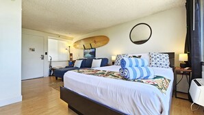 A hotel room with a large bed, a surfboard, and a round mirror on the wall. - 9th Floor Studio Apt, Full kitchen & Insane views! (Honolulu)