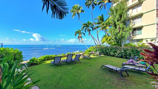 A tropical outdoor area with a view of the ocean, featuring lounge chairs and palm trees. - 9th Floor Studio Apt, Full kitchen & Insane views! (Honolulu)