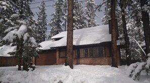 A snow-covered house with a brick exterior and a wooden deck.