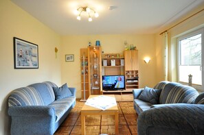 A living room with two sofas, a coffee table, a TV, and a bookshelf. - Ferienwohnung Sonnenblume - Ferienhaus Wempen (Werdum)