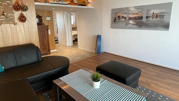 Un salon moderne avec un canapé, un pouf et une table basse, ainsi que des éléments de décoration murale en bois et un tableau encadré.