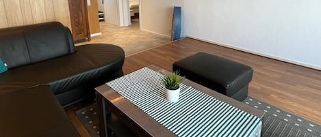 Una sala de estar moderna con un sofá, un reposapiés y una mesa de centro, decoración de pared de madera y una foto enmarcada.