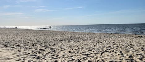 Une plage de sable où l’on peut voir des empreintes menant à l’eau, un ciel dégagé et une jetée qui se profile à l’horizon.