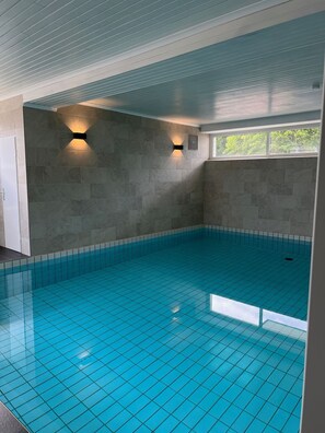 Una piscina interna con pareti e soffitto piastrellati, e due luci a parete.