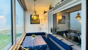 Un espace repas comprenant une table et des bancs, un luminaire suspendu et une vue par la fenêtre.