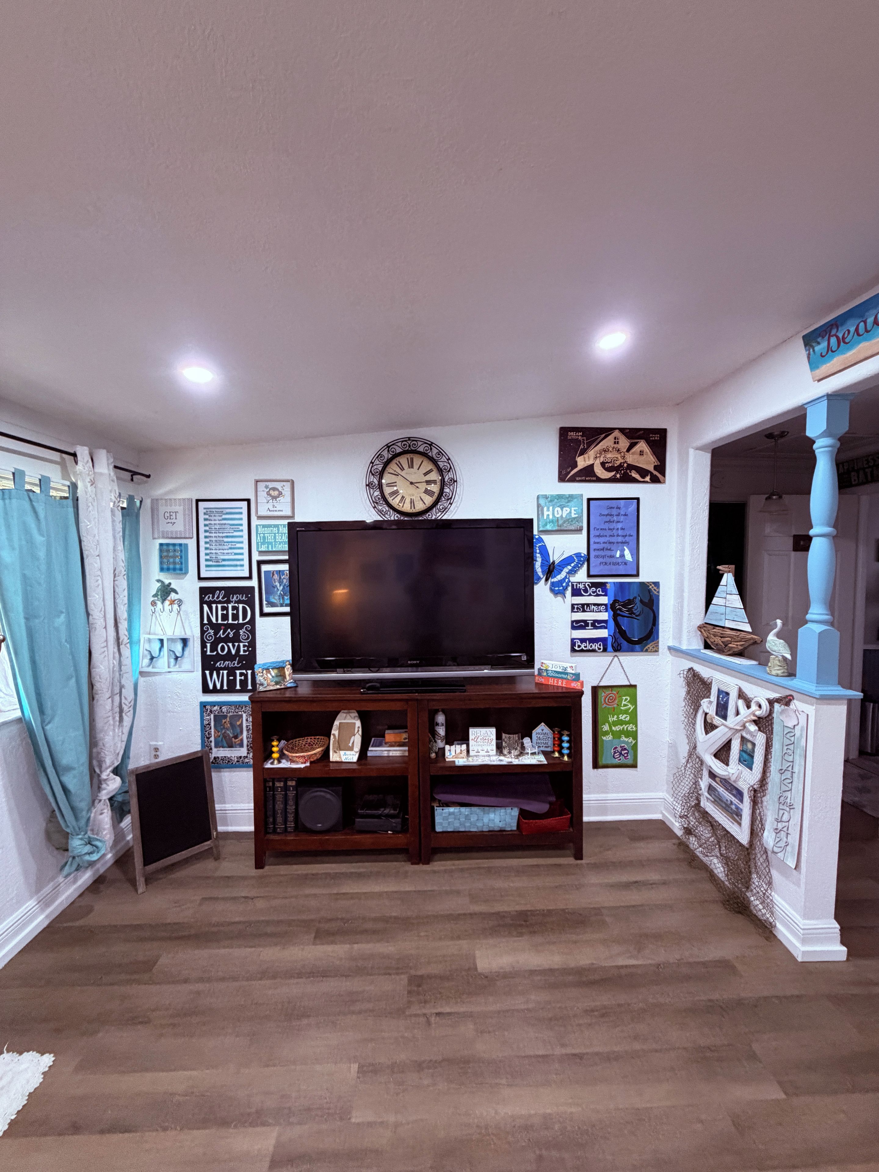 A living room with a flat-screen TV on a wooden stand, surrounded by various wall decorations and a blue accent wall.