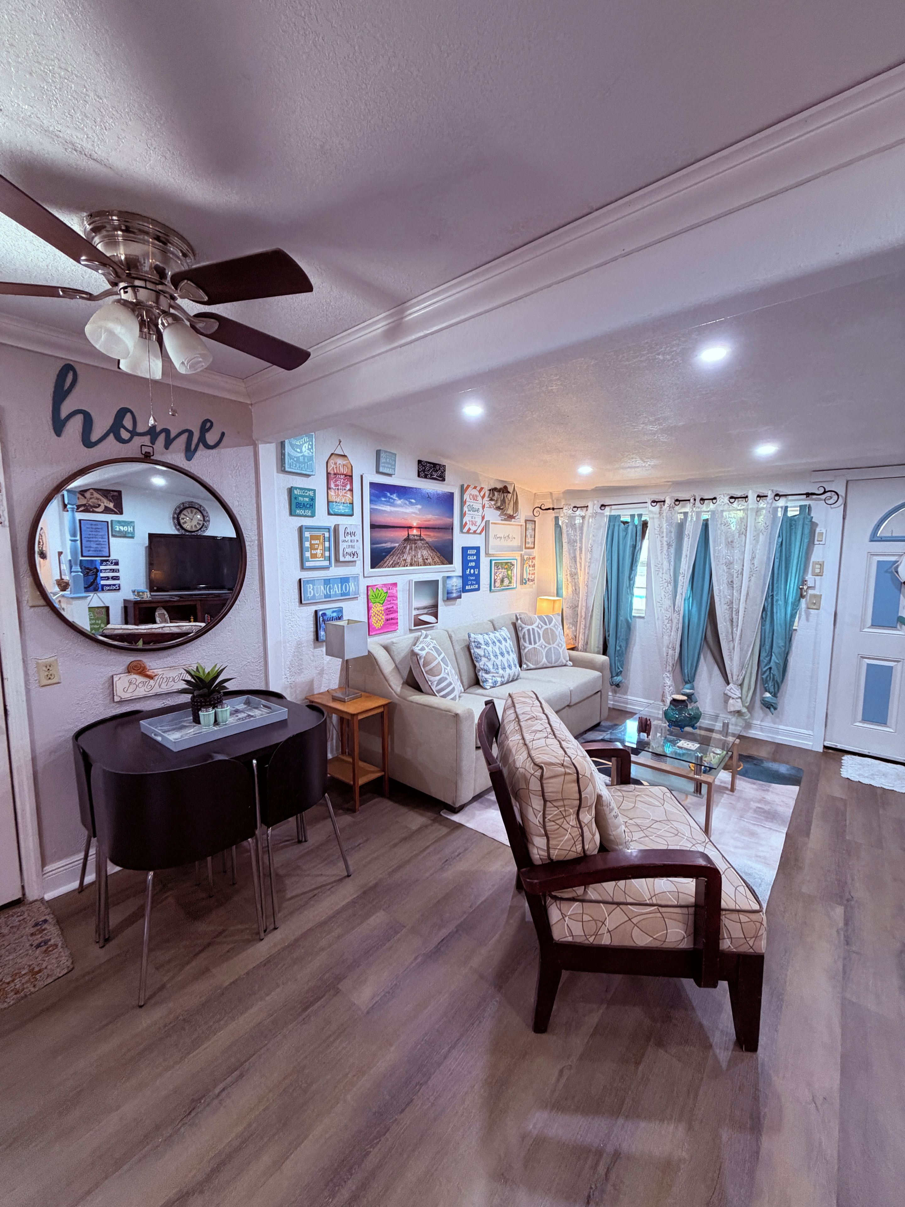 A living room with a ceiling fan, a sofa, a coffee table, a dining table with chairs, and a mirror.