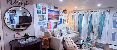A living room with a ceiling fan, a sofa, a coffee table, a dining table with chairs, and a mirror.