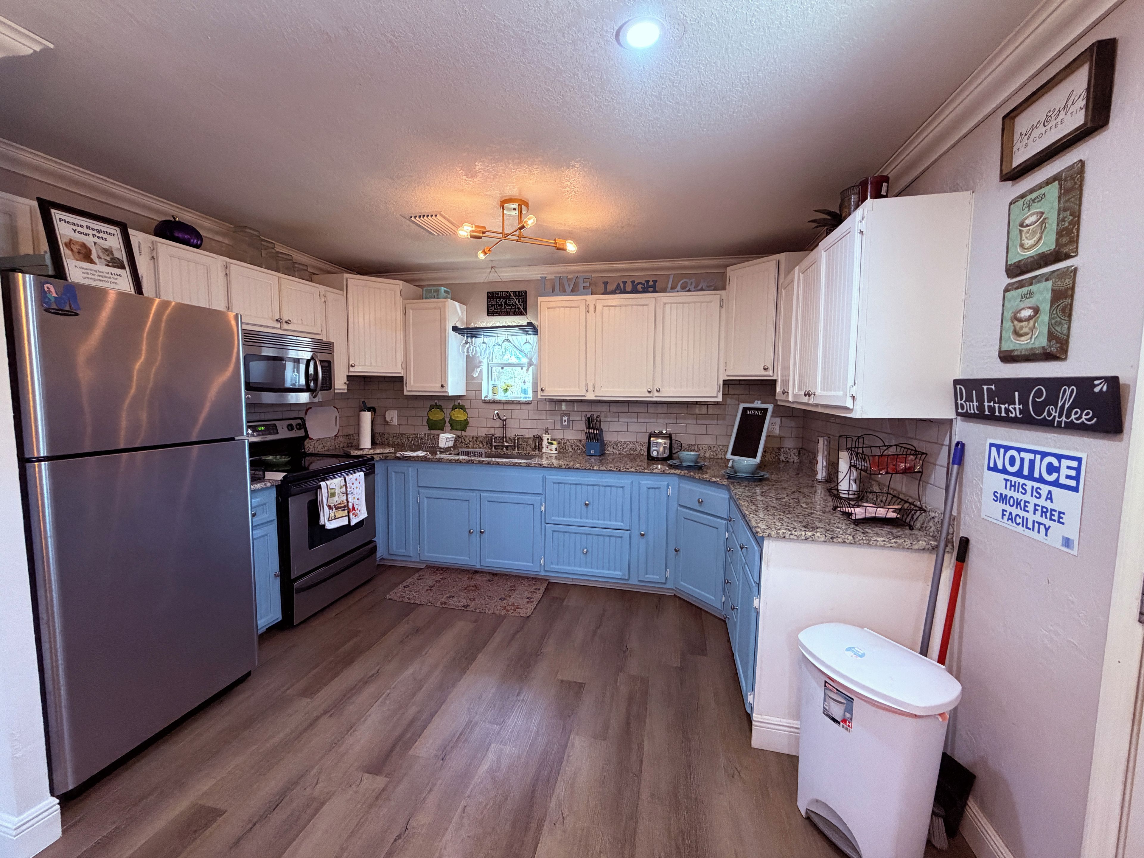 A kitchen with white cabinets, a stainless steel refrigerator, a microwave, and a stove. There is a sign indicating the facility is smoke-free.
