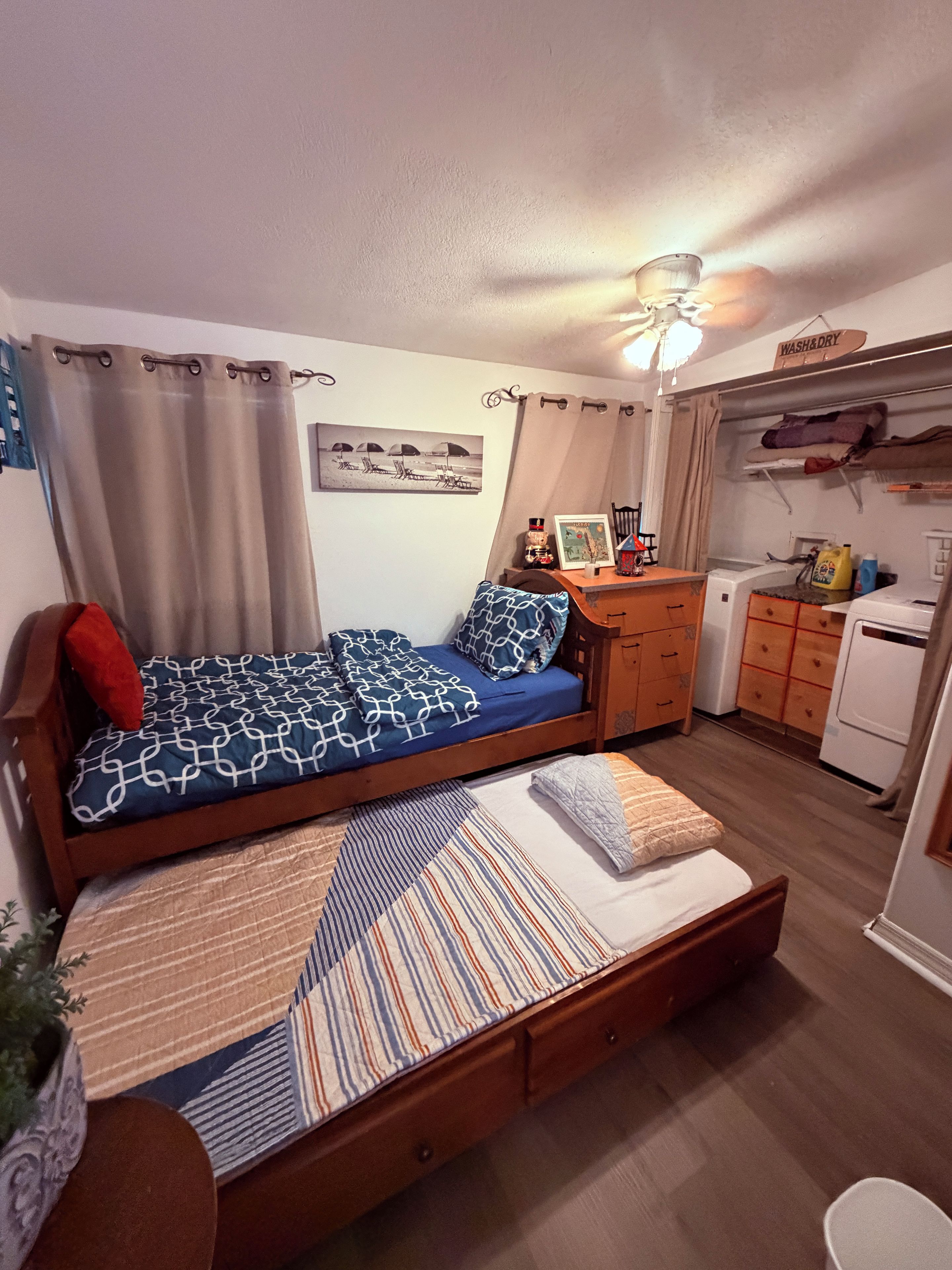 A compact bedroom with a bed, a small desk, a wardrobe, and a washing machine.
