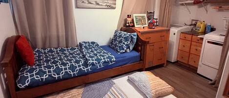 A compact bedroom with a bed, a small desk, a wardrobe, and a washing machine.