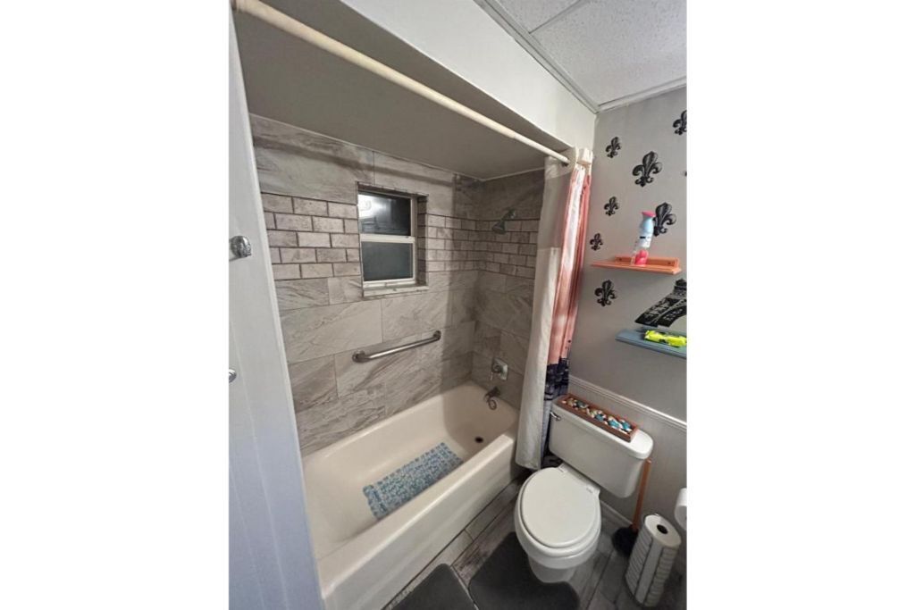 A bathroom with a bathtub, a window, a toilet, and a shower curtain.