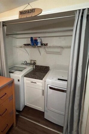 Un cuarto de lavandería pequeño con un lavabo, dos secadoras y un estante con productos de limpieza.