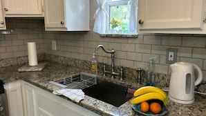 A kitchen with a granite countertop, a sink with a dish rack, a window with white curtains, and a kettle. - Good Location / Good people AND GOOD VIBES ONLY  (Spring Hill)