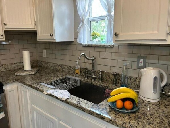 A kitchen with a granite countertop, a sink with a dish rack, a window with white curtains, and a kettle. - Good Location / Good people AND GOOD VIBES ONLY  (Spring Hill)
