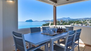 A terrace with a table set for dining, overlooking a coastal cityscape with mountains in the distance. - Bahía del Portet - By Almarina Villas (MORAIRA)