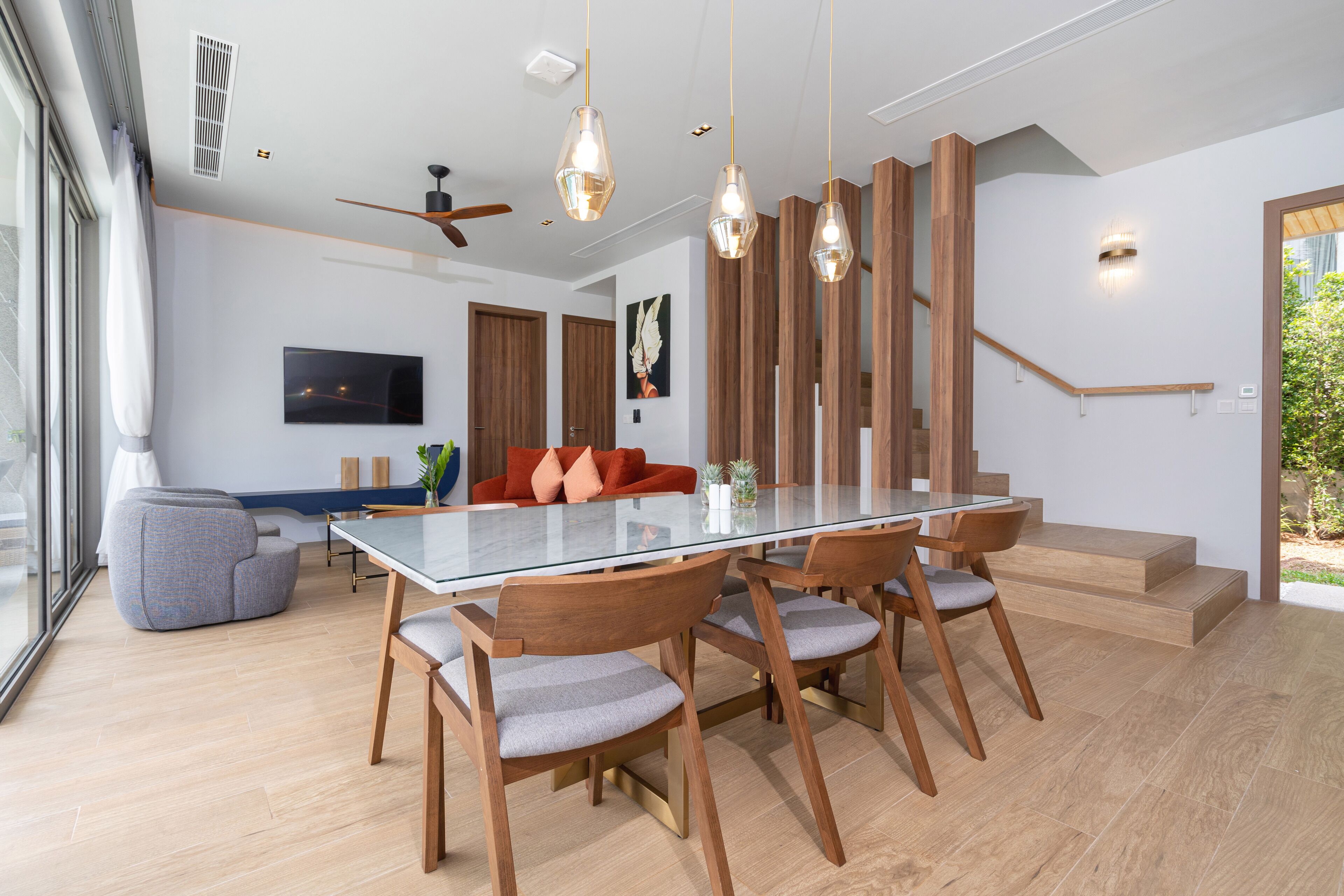 A modern dining area with a glass table, wooden chairs, and pendant lighting.