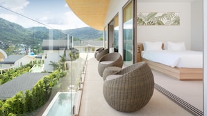 A modern hotel room with a large bed, a glass balcony, wicker furniture, and a view of the mountains. - Himmapana Villas - Hills  (Kamala)