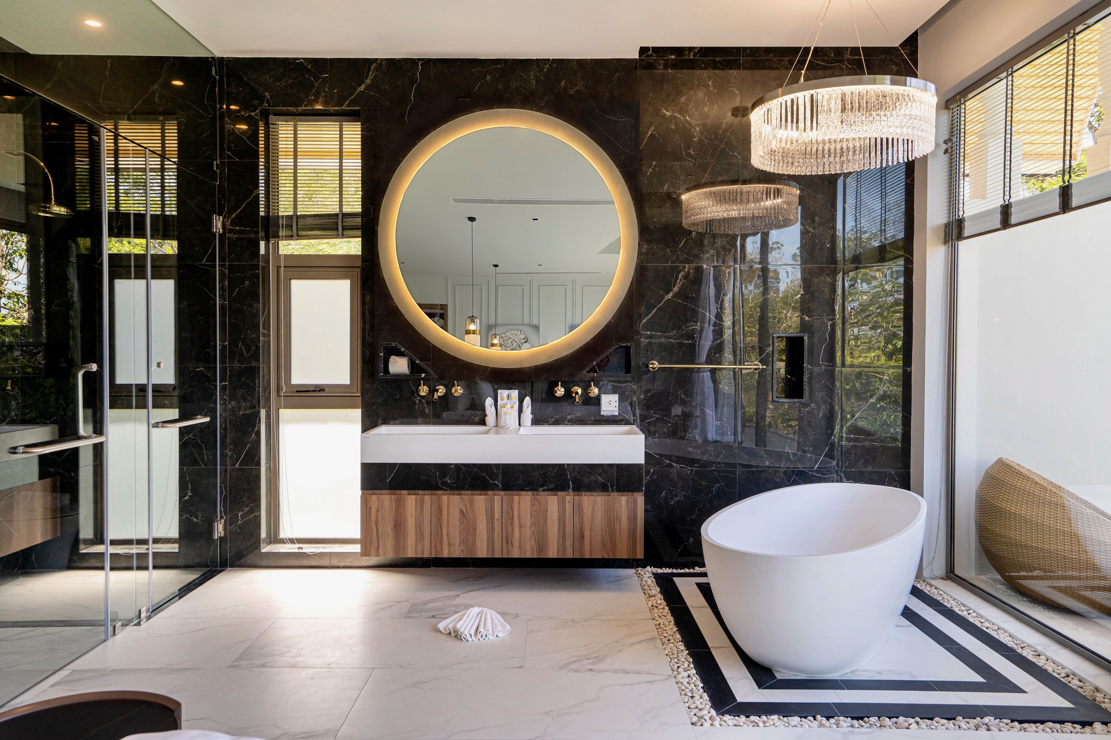 Une salle de bain moderne avec un grand miroir rond, une baignoire sur pieds et une douche séparée par des parois en verre.