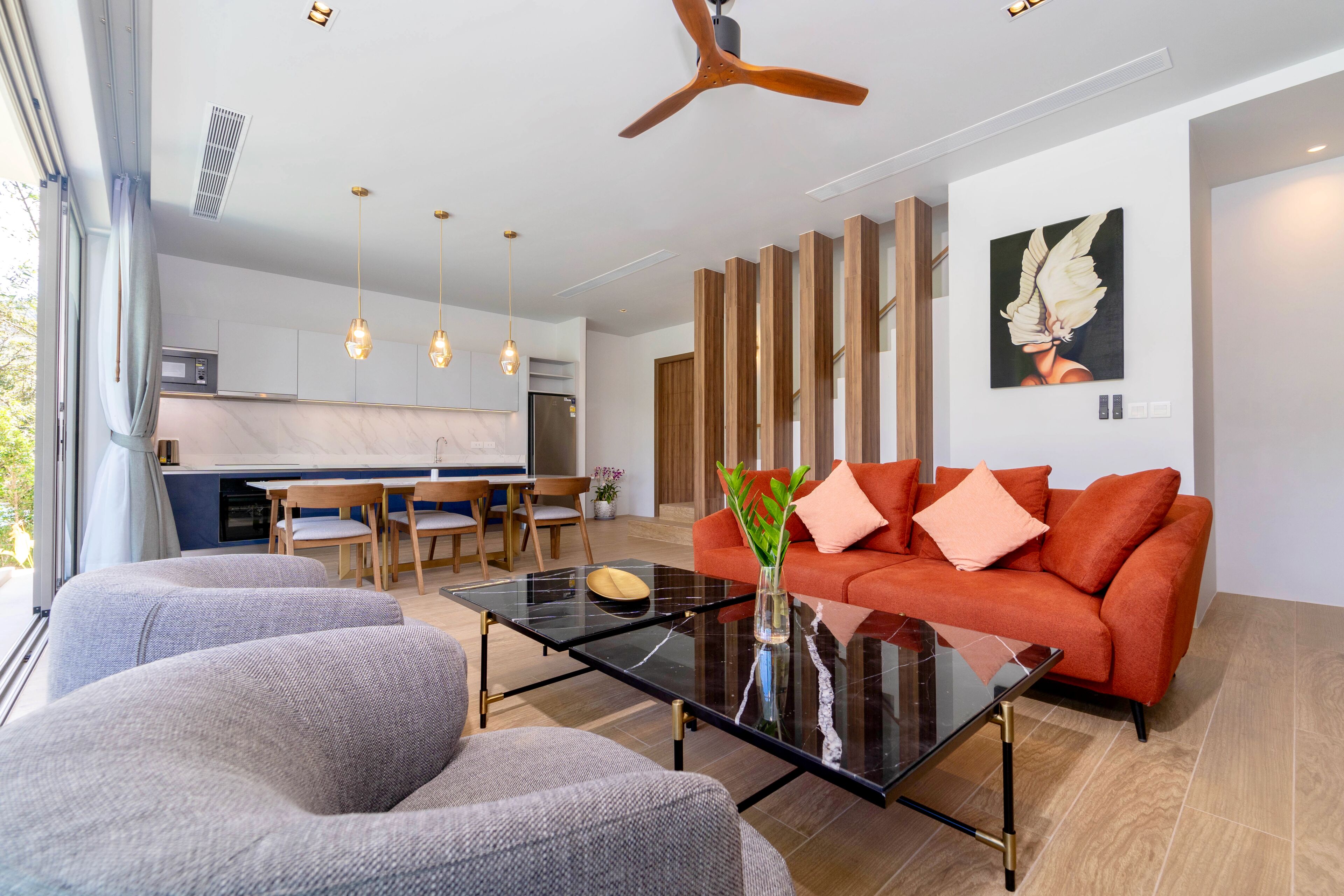 Una sala moderna con una mesa de centro de cristal, sofás grises y un sofá naranja.
