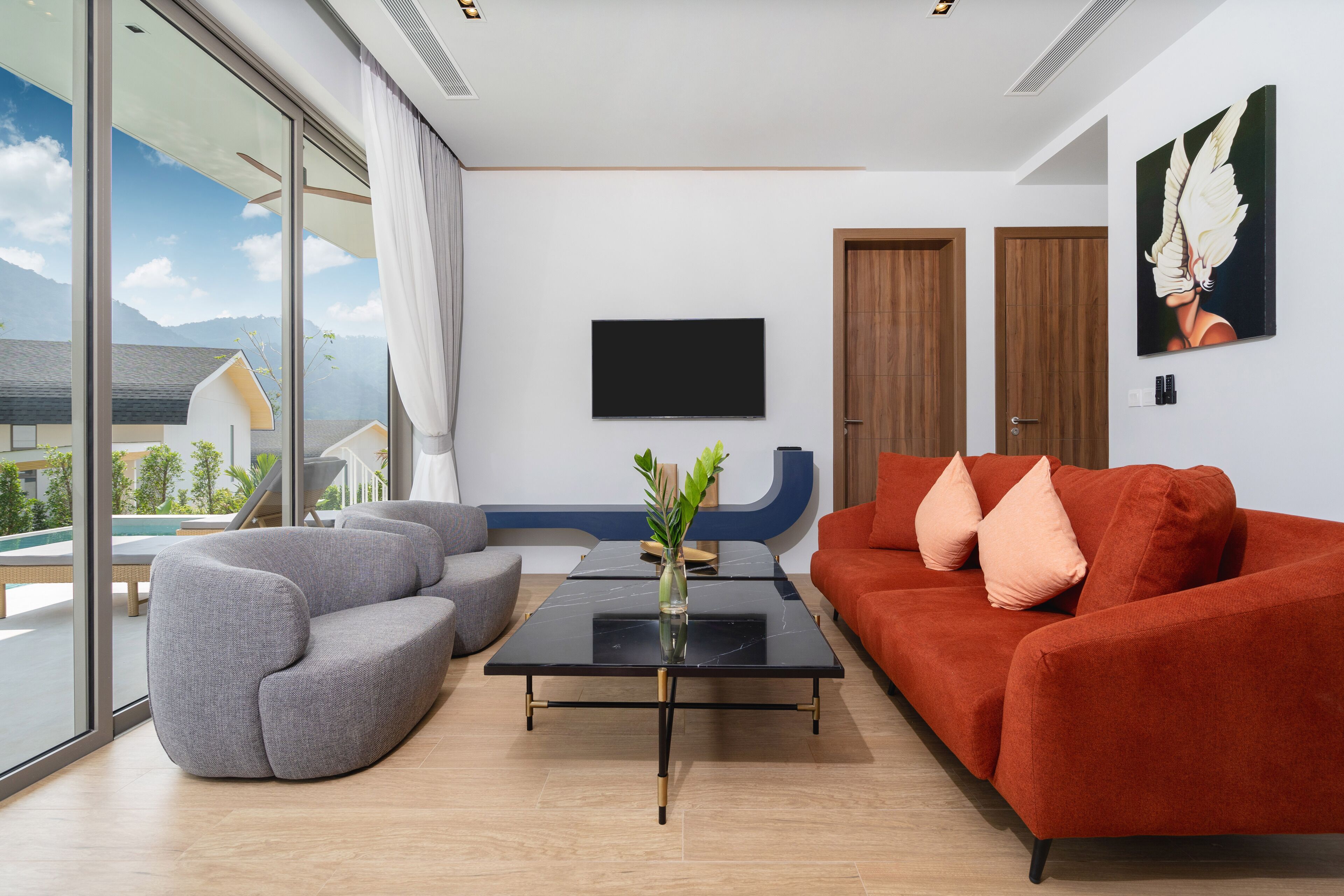 Un salon moderne avec un canapé gris, un canapé rouge et une table basse noire. Un téléviseur est fixé au mur et un tableau est accroché au-dessus du canapé rouge.
