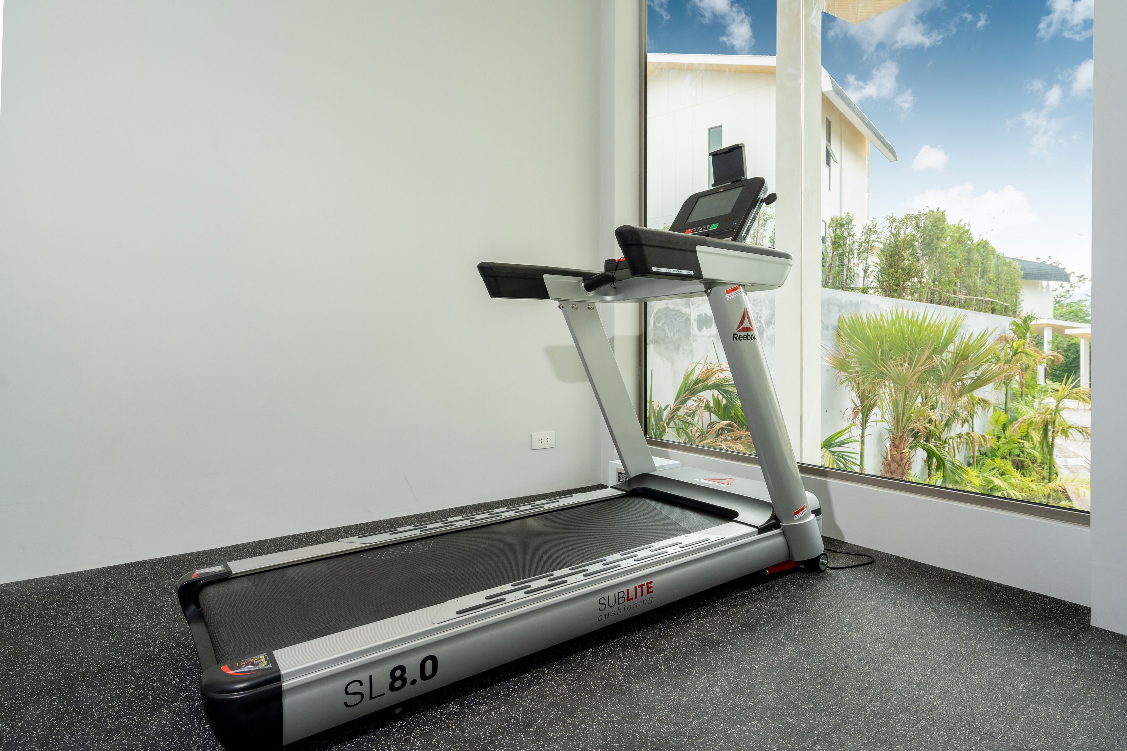 A treadmill in a room with a window overlooking a residential area.
