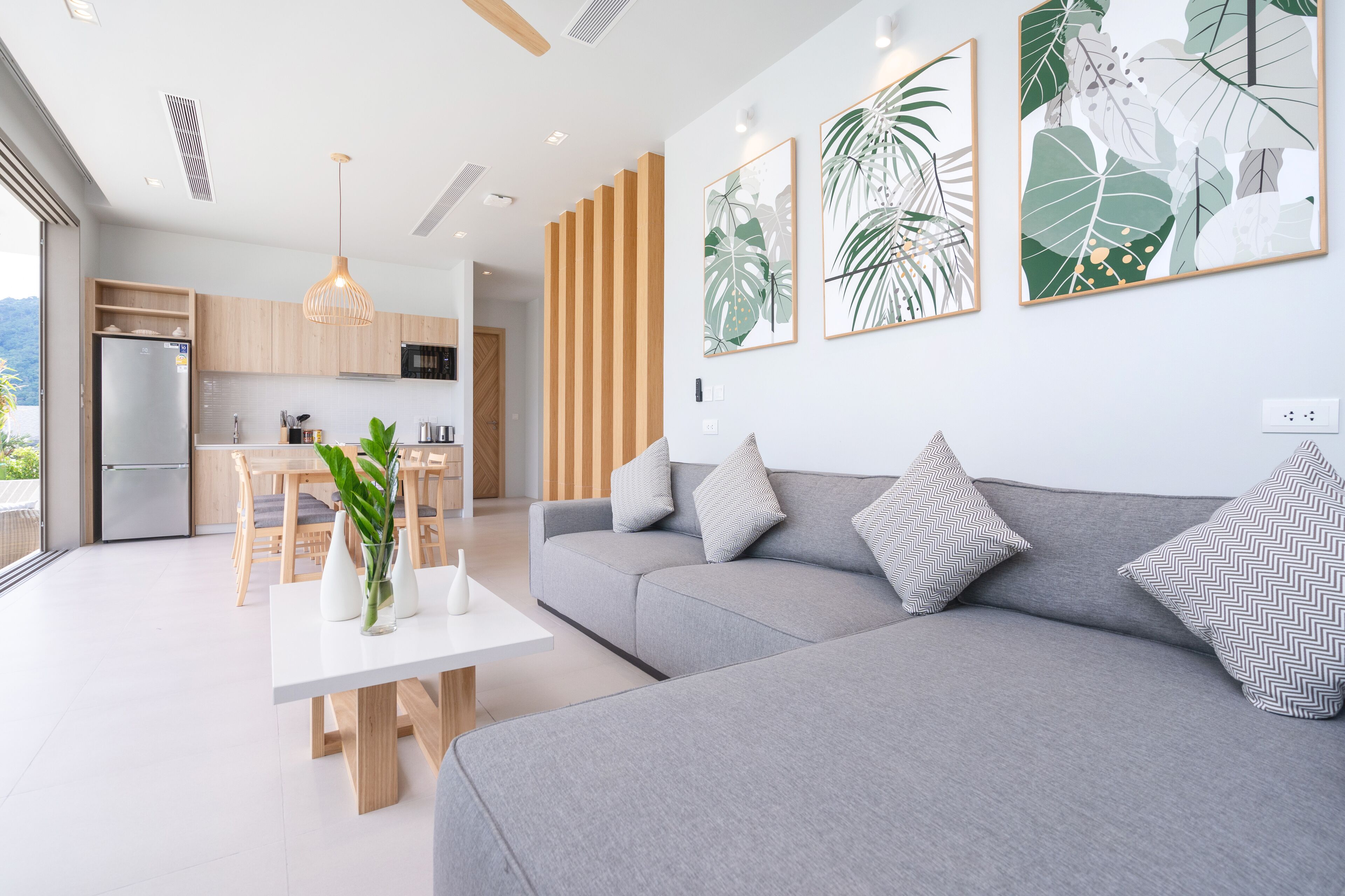 A modern living room with a grey sofa and a dining area with a white table.